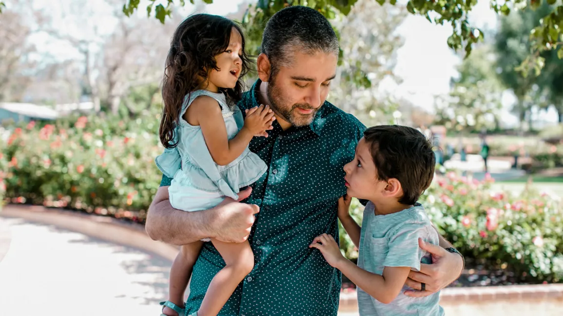 Dad-Standing-Holding-Son-Daughter-Under-Tree-1296X728-header